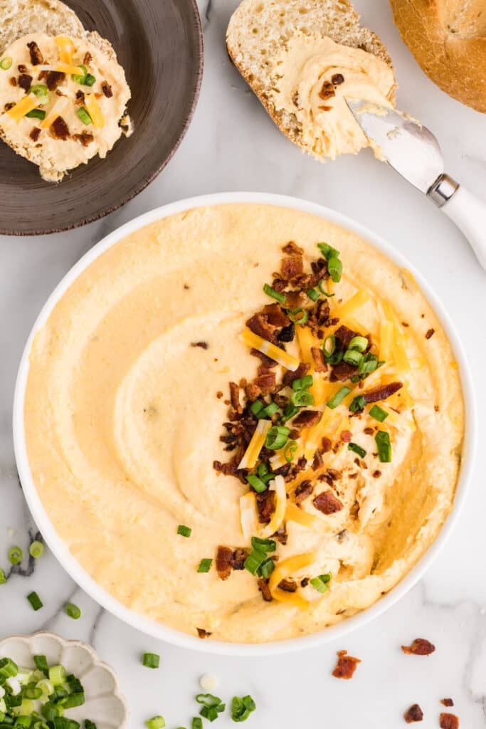 Overhead view of bacon and cheese dip topped with bacon and green onions, served with sliced bread.