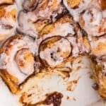 Baking dish of cinnamon rolls with one roll removed.