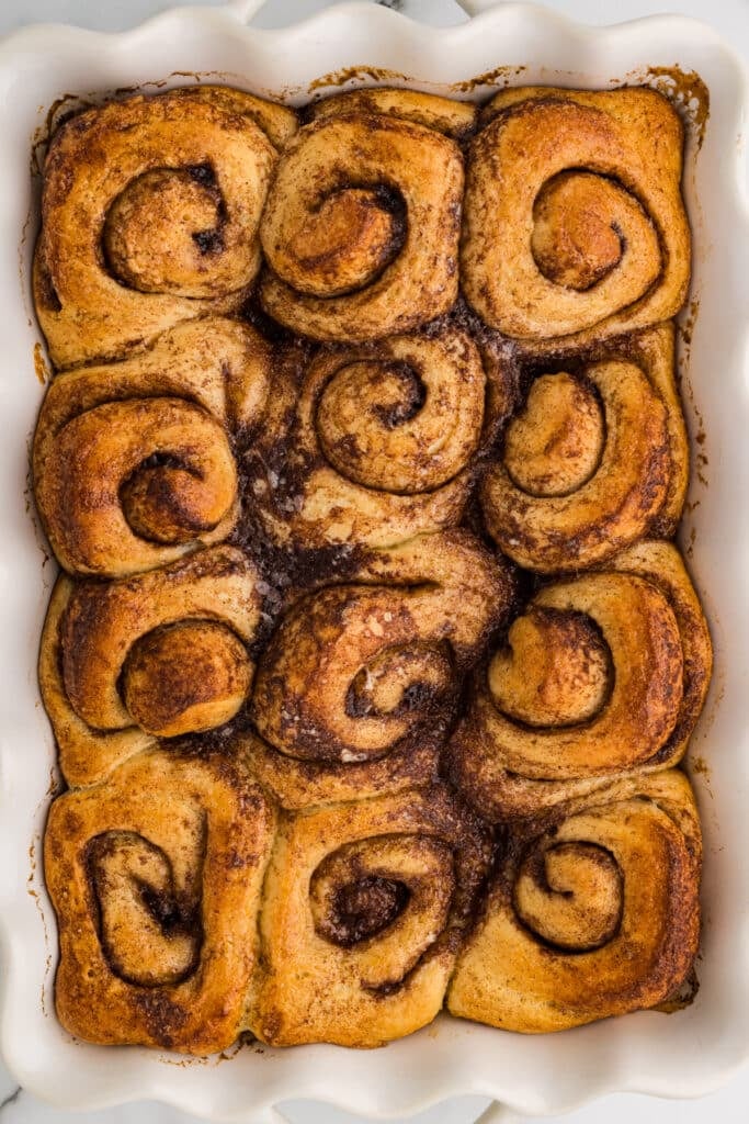 Baked cinnamon rolls arranged in a white ceramic baking dish.