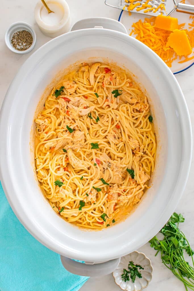 Crockpot filled with creamy chicken spaghetti topped with chopped parsley.