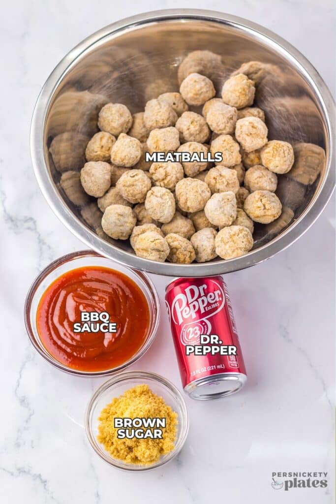 An overhead view of ingredients arranged on a light countertop, including frozen meatballs in a metal bowl, barbecue sauce in a glass bowl, brown sugar in a small dish, and a can of Dr Pepper.