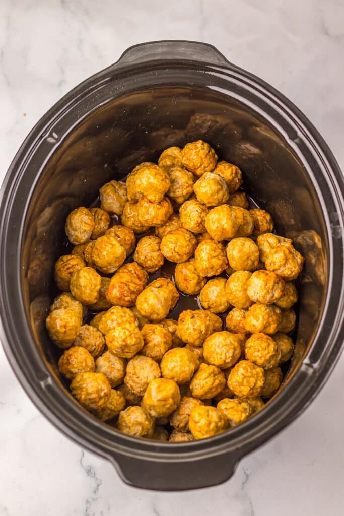 Plain meatballs sitting in a slow cooker with sauce beginning to coat them.