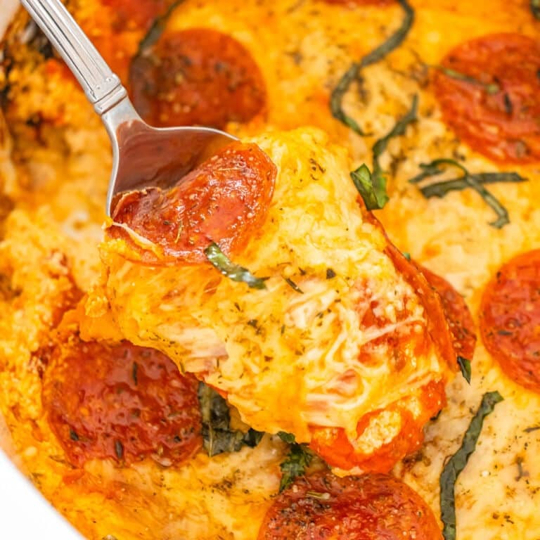 Spoon lifting a cheesy scoop of pizza dip topped with pepperoni.